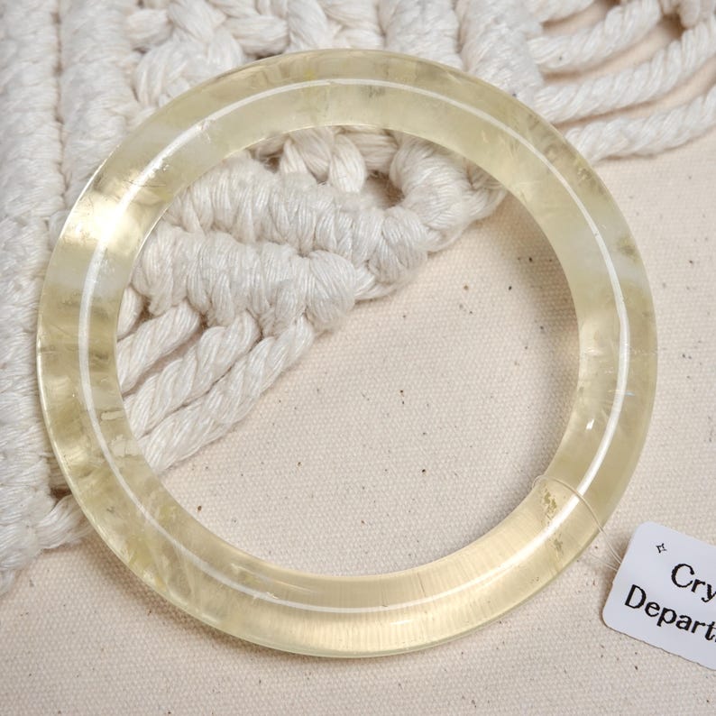May include: A clear, translucent bangle bracelet made of glass or plastic. The bangle is thick and has a smooth, polished finish.