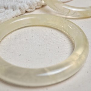 May include: Two translucent white bangle bracelets made of resin. The bracelets are smooth and have a slightly glossy finish.