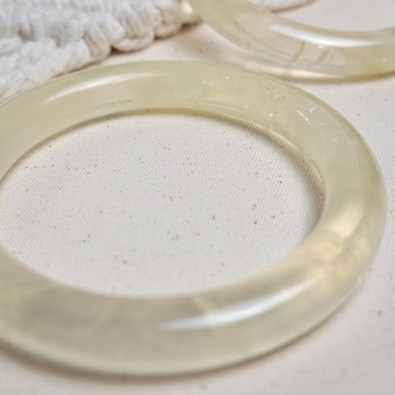 May include: Two translucent white bangle bracelets made of resin. The bracelets are smooth and have a slightly glossy finish.