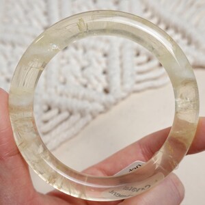 May include: A clear, translucent bangle bracelet made of citrine with gold inclusions. The bracelet is thick and has a smooth, polished finish.