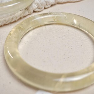 May include: A translucent yellow bangle bracelet made of resin. The bangle is smooth and has a glossy finish.