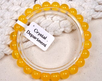 May include: A bracelet featuring vibrant yellow, round beads. The beads are strung together, forming a circular shape. A clear, circular plastic piece is inside the bracelet. A white tag with the text "Crystal Department" is attached.