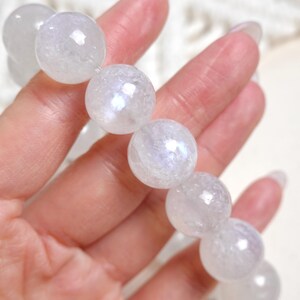 May include: A white gemstone bracelet with iridescent rainbow colours. The bracelet is made of round beads and is shown on a hand.