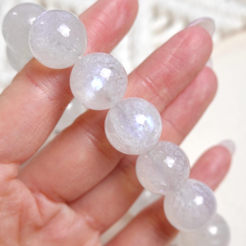 May include: A white gemstone bracelet with iridescent rainbow colours. The bracelet is made of round beads and is shown on a hand.