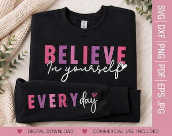 May include: A black crewneck sweatshirt featuring the pink and purple distressed text BELIEVE, followed by the white cursive text In yourself with a small heart. The sleeve displays the pink and purple text EVERY and white cursive day.