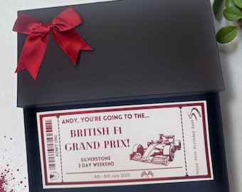 May include: A black gift box with a red satin bow on top. Inside, a ticket for the British F1 Grand Prix at Silverstone, a 3-day weekend event in July 2025, is visible. The ticket is personalized with the text "Andy, you're going to the..."