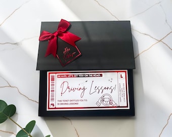May include: A black gift box featuring a red satin bow and a matching tag. Inside, a white ticket with red accents reads: Alex, let's get you on the road... Driving Lessons! This ticket entitles you to: 10 driving lessons! Happy 17th birthday.