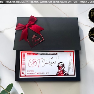 May include: A black rectangular gift box adorned with a dark red satin ribbon and a matching tag. Inside, a white rectangular card features a red and black graphic design with the text CBT Course, a motorcycle helmet, and event details.