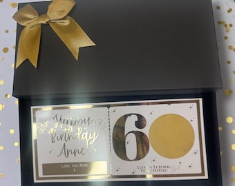 May include: A black gift box with a gold satin bow on top. Inside, a card reads "Happy Birthday Anne! Love You Mum" in gold lettering. The card also features a scratch-off area with the number "60".