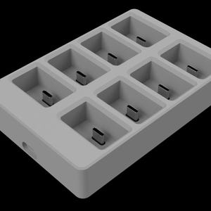 Puede incluir: Una estación de carga de plástico gris con ocho ranuras para cargar dispositivos. Las ranuras están dispuestas en una cuadrícula rectangular.