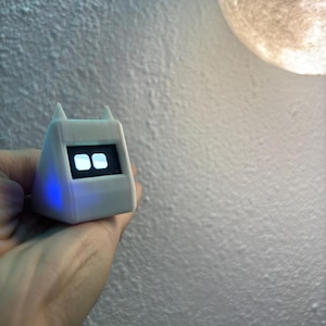 Può includere: Un dispositivo bianco a forma triangolare con un display digitale e luci LED blu. Il dispositivo ha due orecchie arrotondate nella parte superiore.