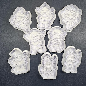 May include: A set of eight white plastic cookie cutters featuring various fantasy characters including fairies, goblins, a wizard, and knights in armor. Each cutter has a detailed outline and internal impression design for shaping dough.