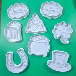 Peut inclure: Ensemble de découpoirs à biscuits en plastique blanc sur le thème de la Saint-Patrick. Les formes comprennent un fer à cheval, un pot d'or, un trèfle, un mug de bière, un chapeau de leprechaun et des découpoirs en forme de nuage avec du texte.