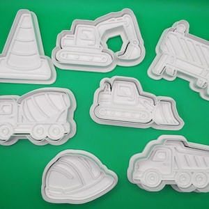 May include: A set of white plastic cookie cutters shaped like construction vehicles and safety equipment. Includes a traffic cone, excavator, barrier, cement mixer, bulldozer, hard hat, and a dumper truck.