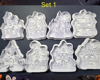 May include: A set of eight white plastic cookie cutters shaped like haunted houses. Each cutter features detailed embossed designs including windows, doors, pumpkins, ghosts, and text such as Boo, Spooky, and Happy Halloween on a dark background.