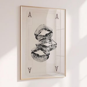 Puede incluir: Impresión artística enmarcada con un diseño de carta de juego, el As de Picas, y tres huellas de labios negros superpuestas. La obra de arte está encerrada en un marco dorado, añadiendo un toque de elegancia.