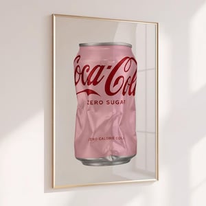 以下が含まれることがあります： 赤いコカ・コーラのロゴ、ZERO SUGARの文字、ZERO CALORIE COLAの文字が前面に印刷された、潰れたライトピンクのアルミ製ソーダ缶が描かれた額装済みのウォールアートプリント。缶の上下の縁はメタリックシルバーです。