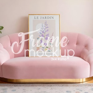 Puede incluir: Un sofá de terciopelo rosa con base dorada sostiene una impresión artística enmarcada. La impresión artística presenta el texto "LE JARDIN" y un diseño floral en morado, amarillo y verde. El sofá está frente a una pared rosa claro.