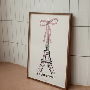 May include: A framed print of a black and white illustration of the Eiffel Tower with a pink bow on top. The text "LA PARISIENNE" is below the tower.