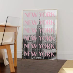 May include: A framed black and white photograph of the New York City skyline, with the Empire State Building prominently featured. The word "NEW YORK" is overlaid in pink, repeated vertically.