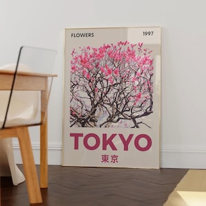 May include: A framed art print featuring a photograph of a flowering tree with pink blossoms. The word "TOKYO" is printed in large, magenta letters below the image, with Japanese characters underneath. The word "FLOWERS" and the year "1997" are printed at the top.