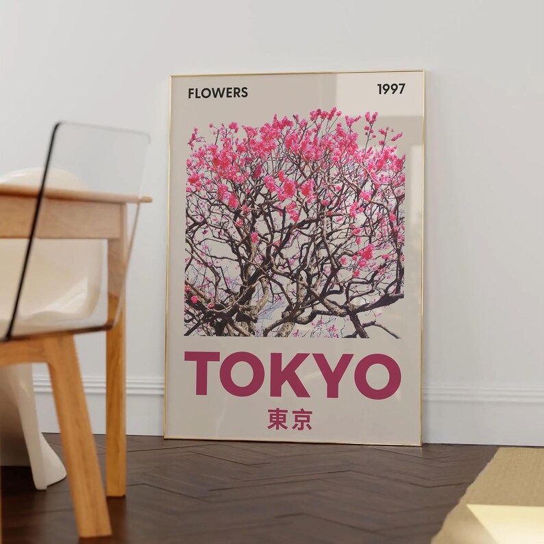 May include: A framed art print featuring a photograph of a flowering tree with pink blossoms. The word "TOKYO" is printed in large, magenta letters below the image, with Japanese characters underneath. The word "FLOWERS" and the year "1997" are printed at the top.