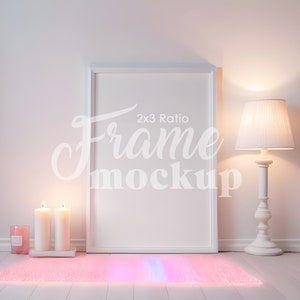 Puede incluir: Maqueta de marco de imagen blanco con una proporción de 2x3, sentado sobre una superficie blanca con una luz rosa y azul que se refleja en la superficie. Hay dos velas blancas y una vela rosa en una bandeja blanca delante del marco. Una lámpara blanca con una pantalla blanca está a la derecha del marco.