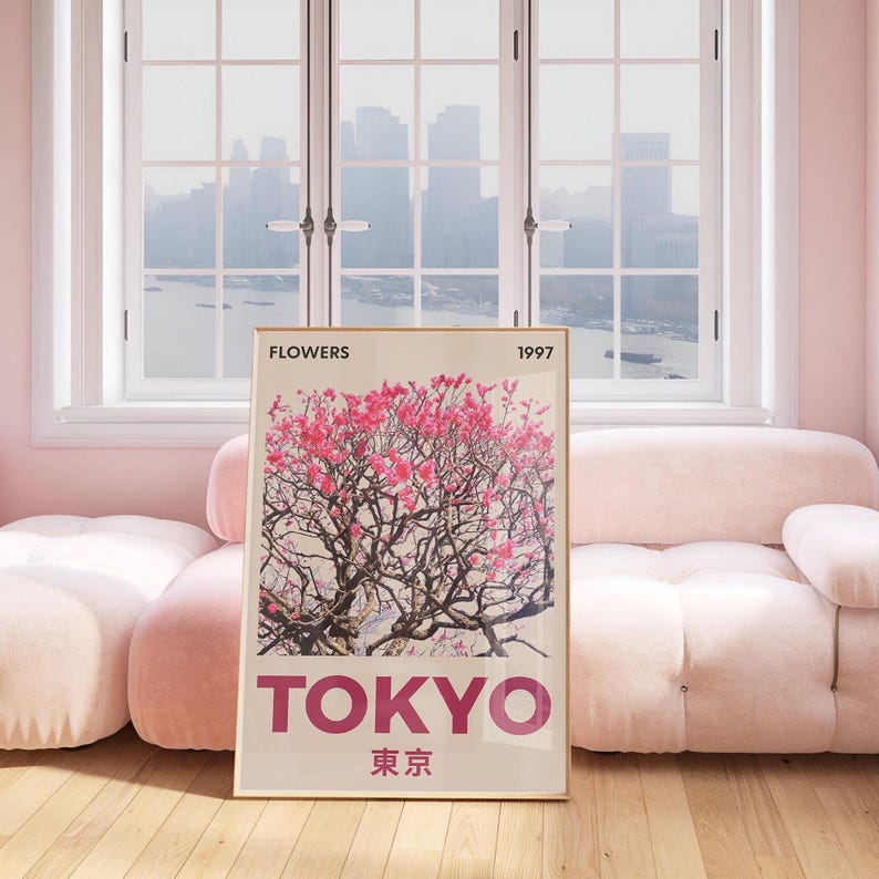 May include: A framed art print featuring a pink flowering tree with the word "TOKYO" in large, bold letters. The print also includes the Japanese characters for Tokyo, the word "FLOWERS", and the year "1997". The artwork is displayed in a room with a pink sofa and a window.