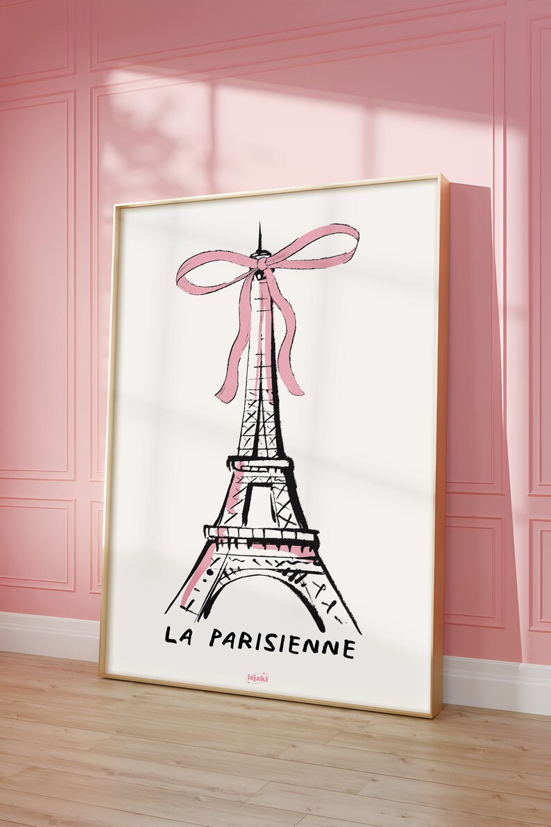 May include: A black and white illustration of the Eiffel Tower with a pink bow on top. The text "LA PARISIENNE" is below the tower. The image is framed in gold.