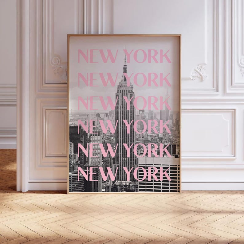 May include: A framed black and white photograph of the New York City skyline, featuring the Empire State Building. The word "NEW YORK" is repeated in pink over the image. The frame is gold.
