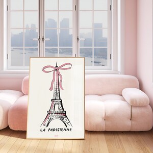 May include: A framed print of a black and white illustration of the Eiffel Tower with a pink bow on top. The text "LA PARISIENNE" is printed below the tower. The print is hanging on a wall in a room with a pink sofa.
