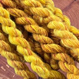 May include: Close-up of several skeins of yellow and orange yarn. The yarn is twisted and has a textured appearance. The colors blend together, creating a warm, inviting look. The yarn is likely used for knitting or crocheting projects.