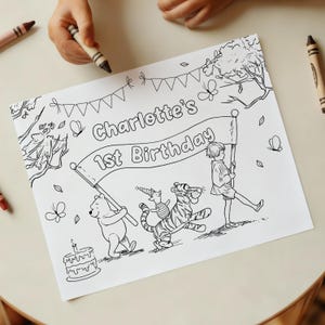 Op de afbeelding: Zwart-wit kleurplaat met Winnie de Poeh-personages, een banner met de tekst "Charlotte's 1st Birthday" en een taart. Kinderhanden houden een kleurpotlood vast, klaar om de pagina in te kleuren.