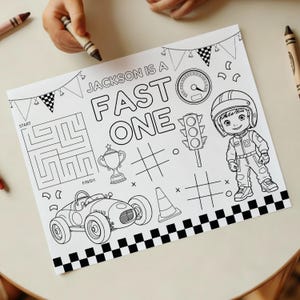 May include: Black and white coloring page with the text "JACKSON IS A FAST ONE". The page features a race car, a race car driver, a maze, a trophy, a traffic light, and a checkered flag border. Crayons are visible.