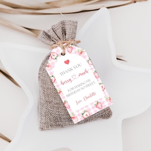 May include: A small hessian gift bag tied with twine, with a tag featuring a pink gingham pattern and strawberry illustrations. The tag reads "Thank You berry much" and "For making my birthday so sweet."
