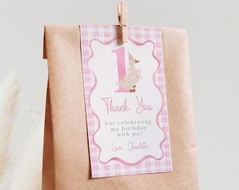 May include: A brown paper bag with a pink and white gingham tag. The tag features a cartoon goose wearing a party hat, the number 1, and the words "Thank You." The tag is held by a wooden clip.