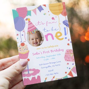 Könnte beinhalten: Eine farbenfrohe Geburtstagseinladung mit dem Text "it's fun to be one!" und "Sofia's First Birthday." Die Einladung zeigt Illustrationen von Luftballons, einem Cupcake, einer Torte und einem Geschenk. Ein Foto eines lächelnden Babys befindet sich in der Mitte.