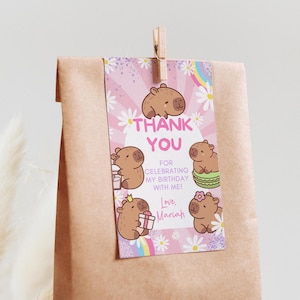 May include: A brown paper gift bag with a decorative tag. The tag features cartoon capybaras, daisies, and a rainbow. Text on the tag reads "THANK YOU" and "FOR CELEBRATING MY BIRTHDAY WITH ME!" with the name "Mariah".