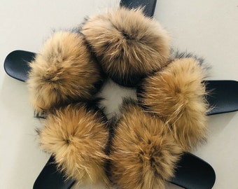 May include: Five pairs of black slide sandals with large, fluffy, brown fur accents. The fur appears to be a mix of light and dark brown tones, creating a textured appearance. The sandals are arranged in a star-like pattern.