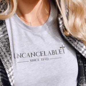May include: A gray t-shirt with the text "Uncancelable - Since 33AD" and a cross graphic.