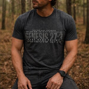 May include: Dark gray t-shirt with the text "TAKE YOUR GEAR, YOUR QUIVER, AND YOUR BOW, AND GO OUT TO THE FIELD AND GENESIS 27:3 HUNT GAME FOR ME" in a distressed font. The shirt is short-sleeved and has a crew neck.