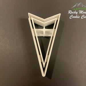 May include: White plastic cookie cutter shaped like a pointed arrow with a star in the center. The cookie cutter is for making cookies in the shape of the Pontiac logo.