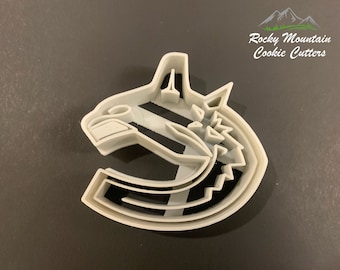 May include: A white plastic cookie cutter shaped like a hockey team logo. The logo features a stylized wolf's head with a hockey stick and a letter C. The text "Rocky Mountain Cookie Cutters" is visible in the upper right corner of the image.