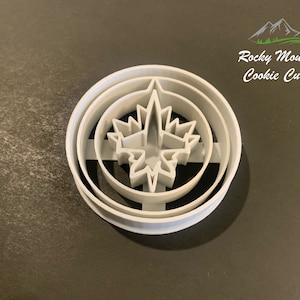 May include: White plastic cookie cutter shaped like a stylised starburst with three concentric circles. The cookie cutter is for making cookies in the shape of a starburst.