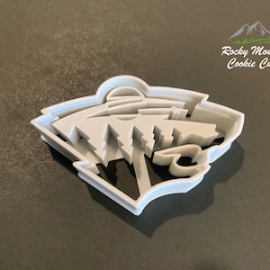 May include: A white plastic cookie cutter shaped like the logo of the NHL's Arizona Coyotes. The logo features a stylised coyote head with a mountain range in the background. The cookie cutter is made by Rocky Mountain Cookie Cutters.