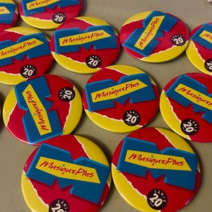 May include: A collection of round, red, yellow, and blue buttons with the text "Musique Plus" and the number "20" on them.