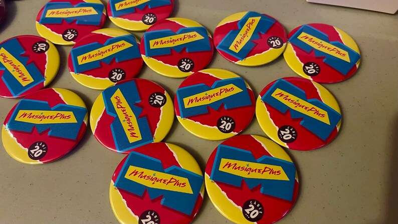 May include: A collection of round, red, yellow, and blue buttons with the text "Musique Plus" and the number "20" on them.