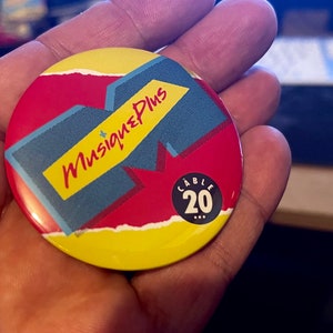 May include: A yellow, red and blue round button with the text "Musique Plus" and "Cable 20" in black.