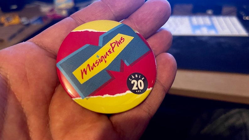 May include: A yellow, red, and blue round button with the text "Musique Plus" and "Cable 20" in black.