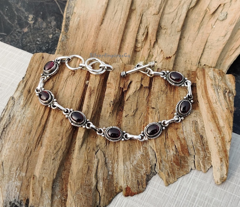 May include: A silver bracelet with a toggle clasp and oval-shaped red gemstones.